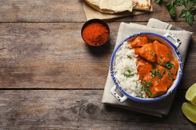 Photo of Delicious butter chicken with rice served on wooden table, flat lay. Space for text