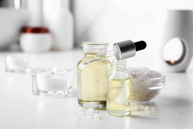 Photo of Essential oils, sea salt and candles on white table in bathroom, closeup