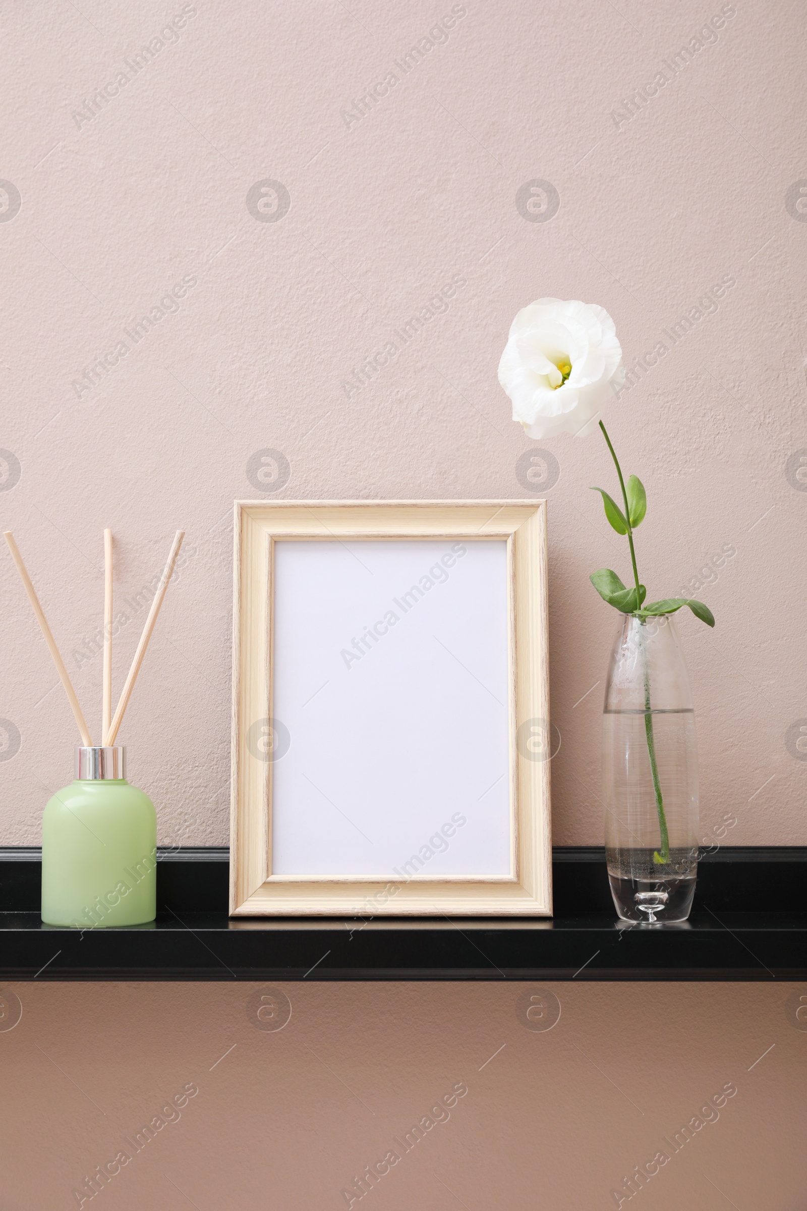 Photo of Empty photo frame, air reed freshener and beautiful flower on shelf near pink wall