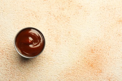 Photo of Tasty barbeque sauce in bowl on beige textured table, top view. Space for text