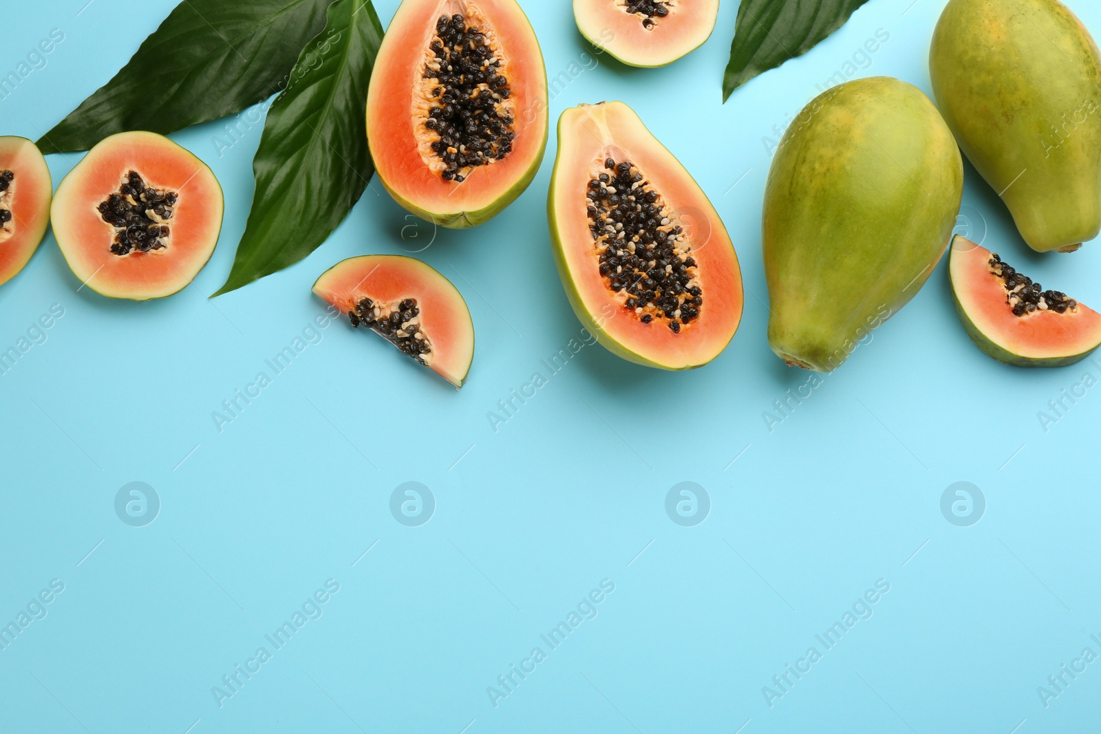 Photo of Fresh ripe papaya fruits with green leaves on light blue background, flat lay. Space for text