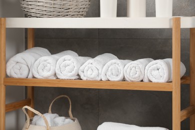 Photo of Wooden shelf and wicker basket with soft terry towels in bathroom