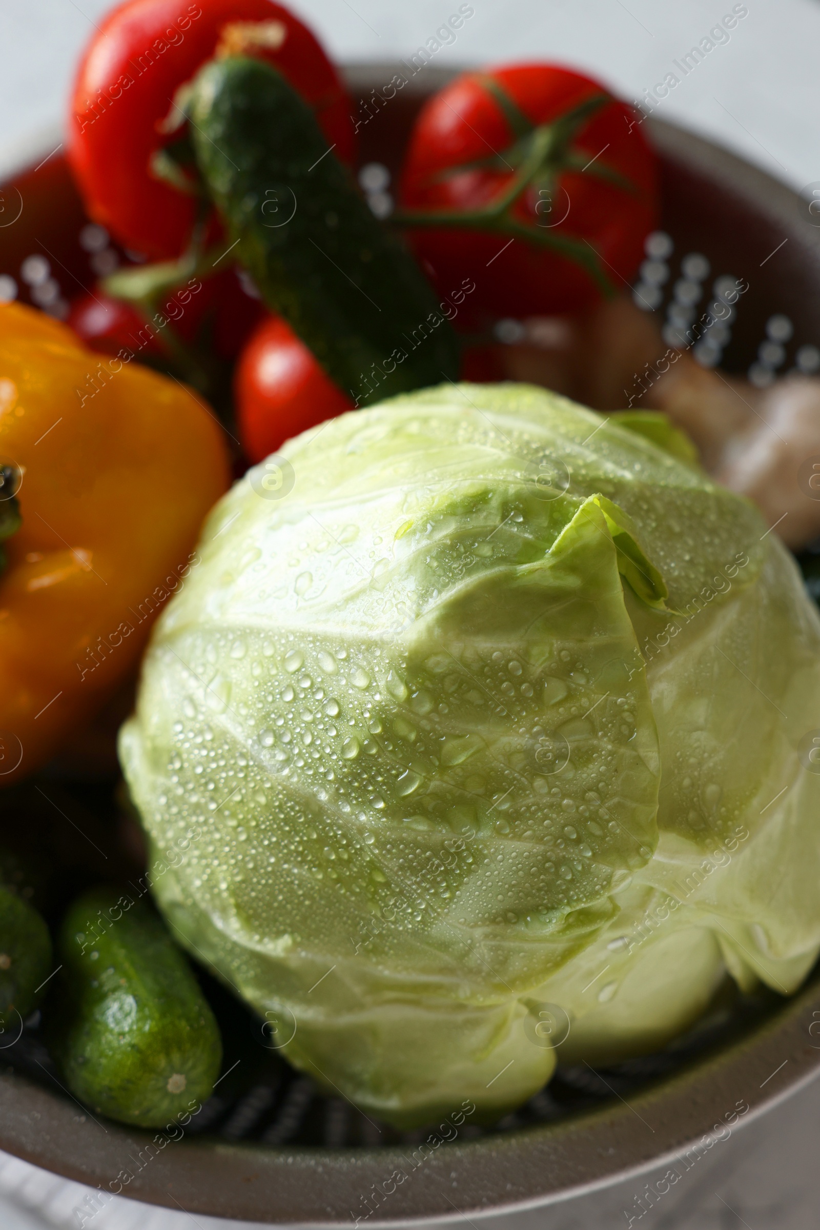 Photo of Metal colander with different wet vegetables on white textured table, above view