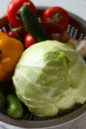 Metal colander with different wet vegetables on white textured table, above view