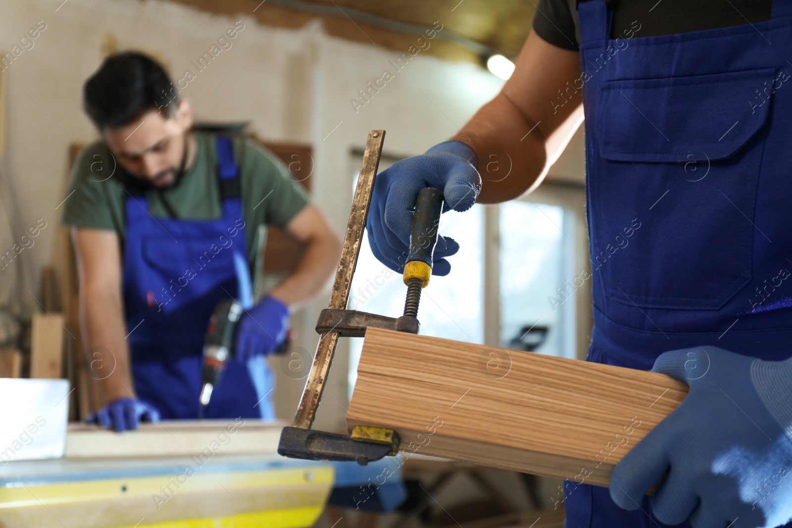 Photo of Professional carpenter with wooden board and clamp in workshop, closeup