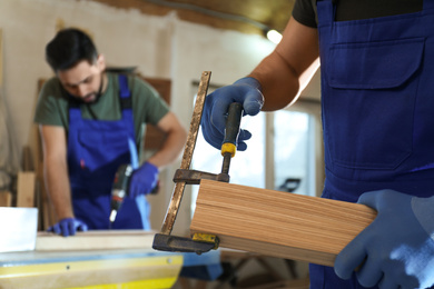 Professional carpenter with wooden board and clamp in workshop, closeup