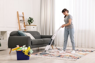 Photo of Happy young housewife vacuuming rug at home