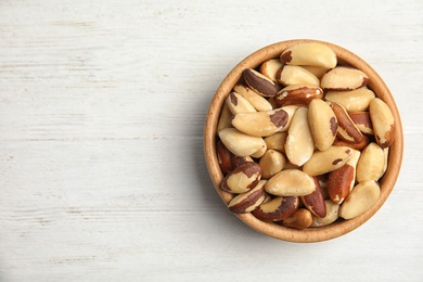 Photo of Bowl with tasty Brazil nuts and space for text on white wooden background, top view