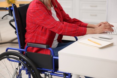 Photo of Woman in wheelchair using computer at table indoors, closeup