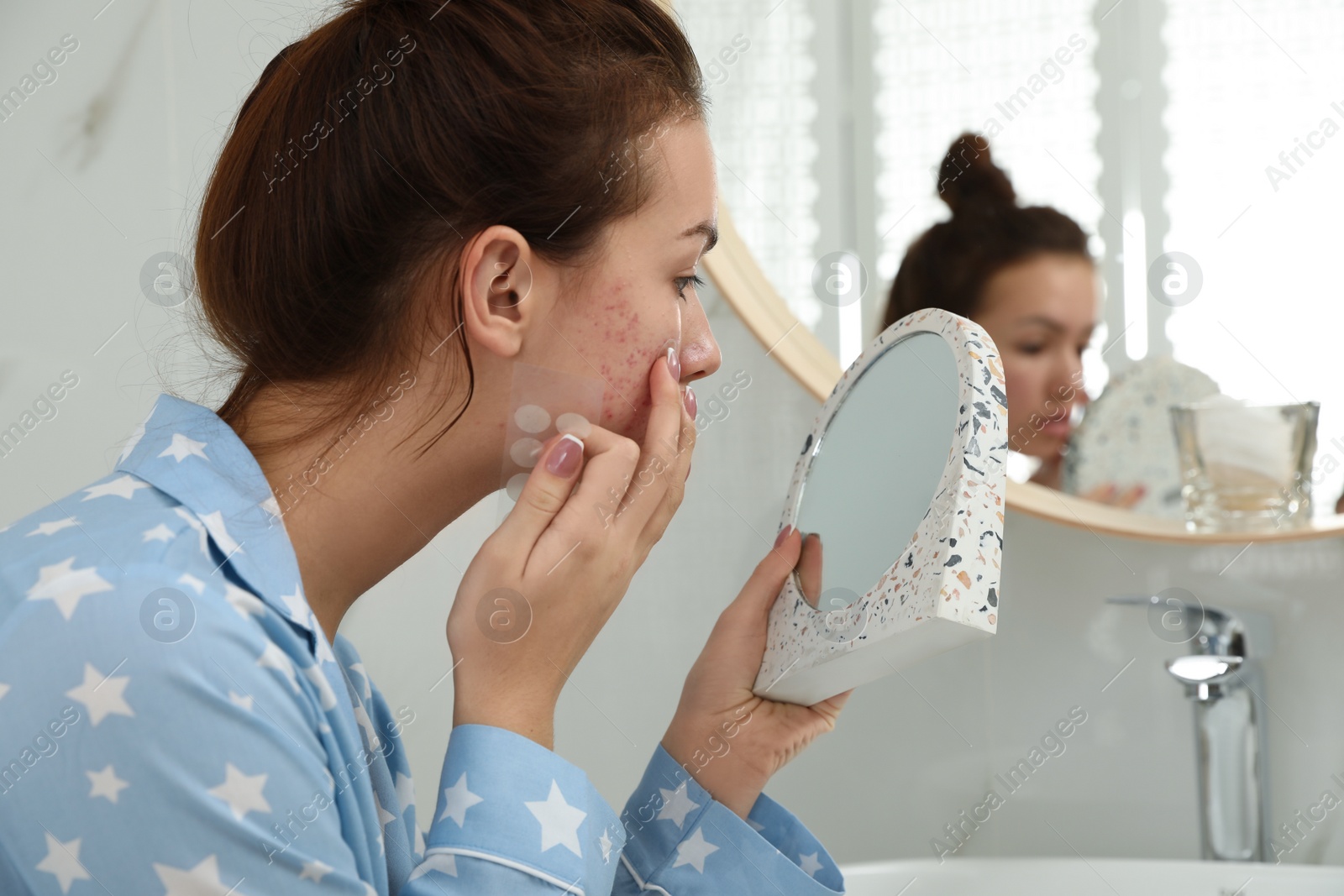 Photo of Teen girl applying acne healing patch using mirror in bathroom