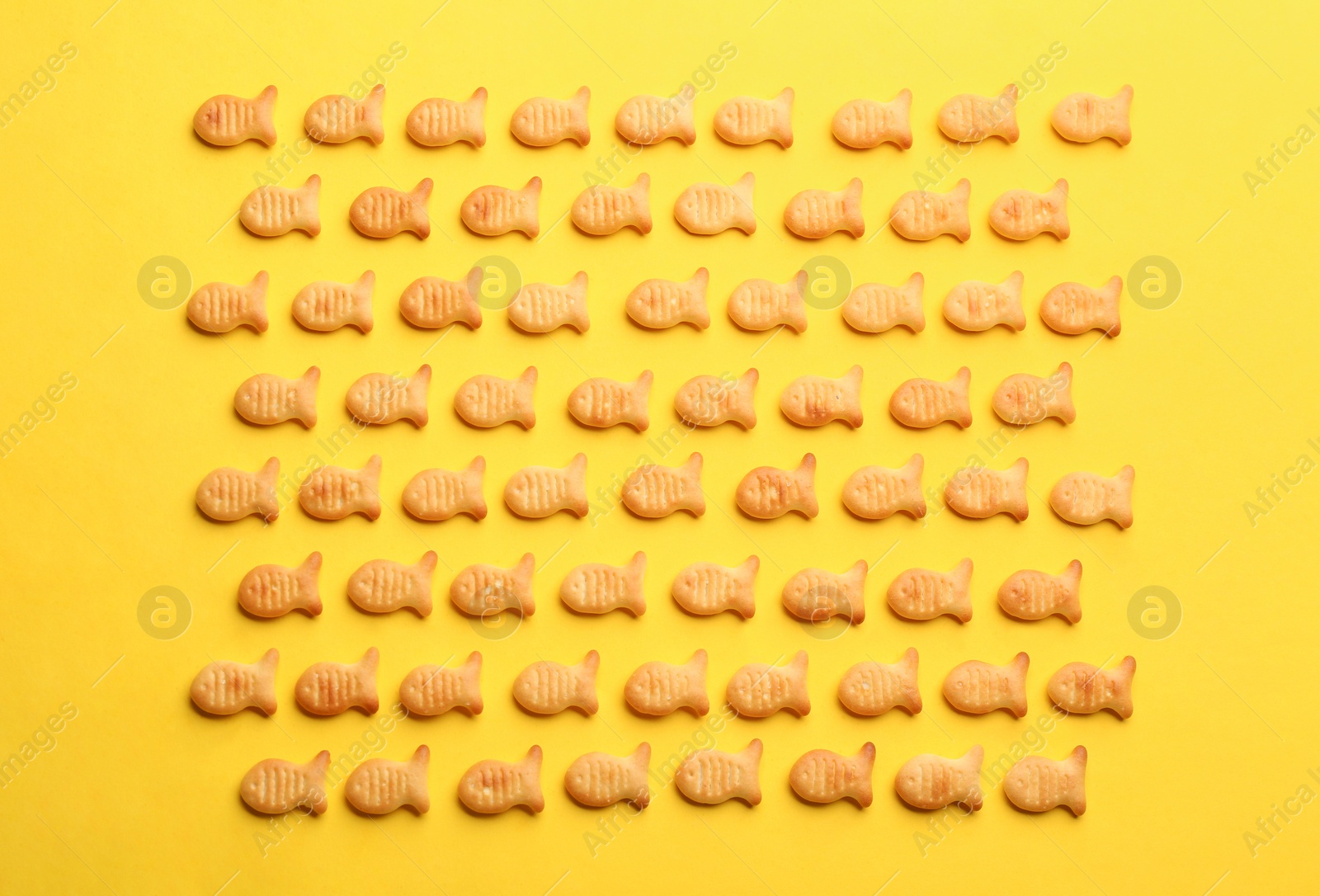 Photo of Delicious goldfish crackers on yellow background, flat lay