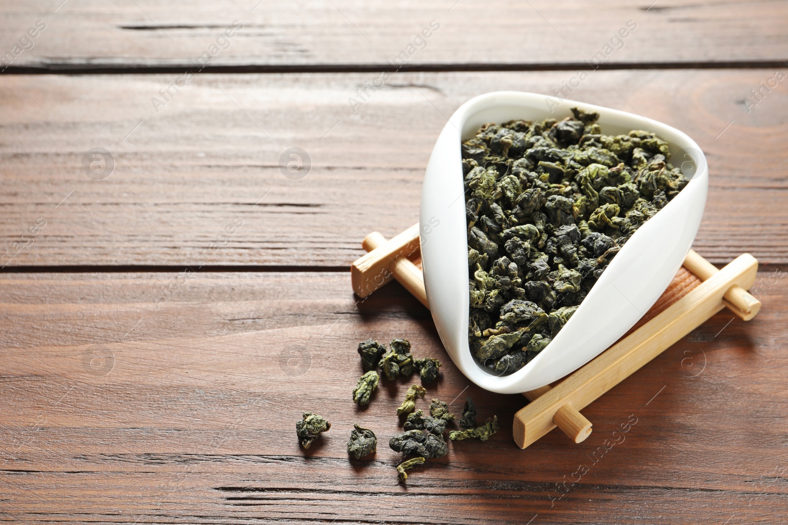 Photo of Chahe with Tie Guan Yin oolong tea leaves on wooden table. Space for text