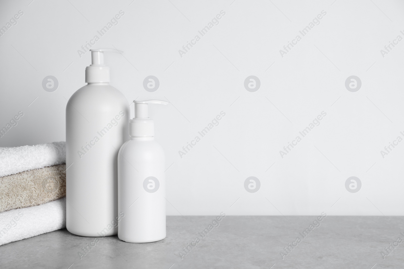 Photo of Bottles of cosmetic products and towels on grey table. Space for text