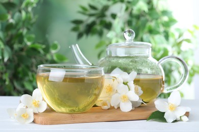 Photo of Tasty tea and fresh jasmine flowers on white wooden table