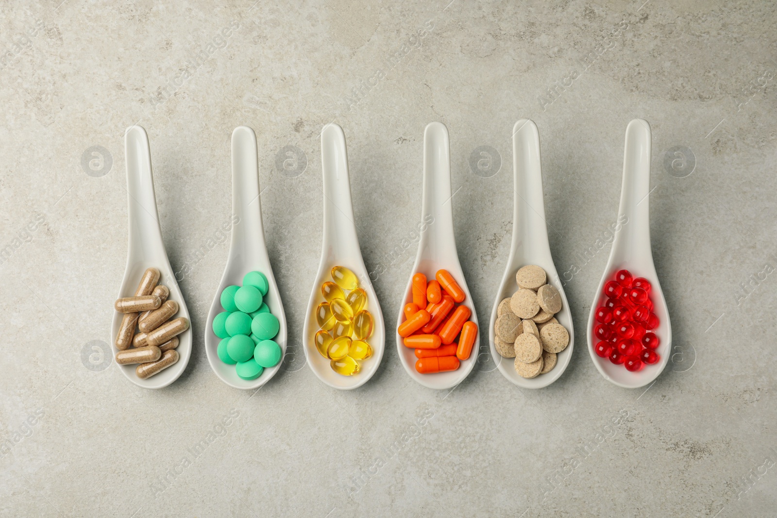 Photo of Spoons with different dietary supplements on light grey table, flat lay