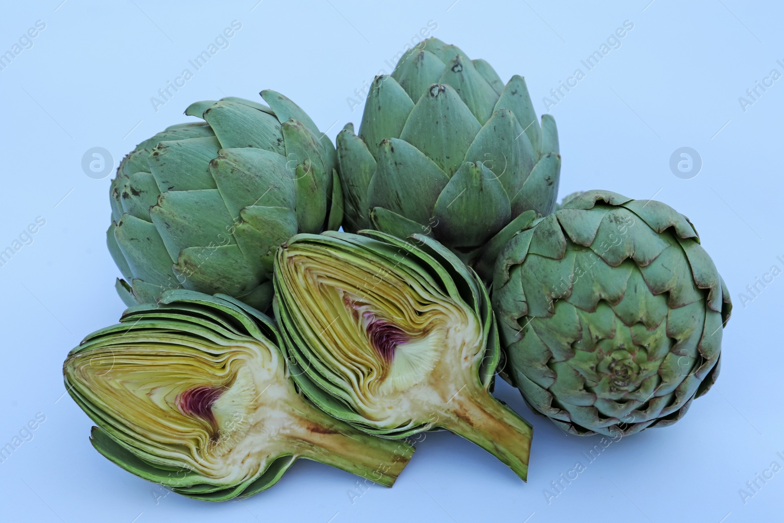 Photo of Cut and whole fresh raw artichokes on light blue background, closeup