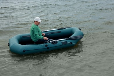 Photo of Man fishing with rod from inflatable rubber boat on river