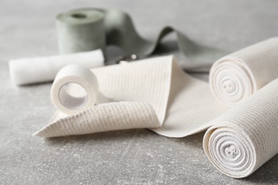 Photo of Medical bandage rolls and sticking plaster on grey table, closeup