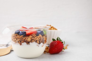 Photo of Tasty granola with berries and yogurt in plastic cup on light table, space for text