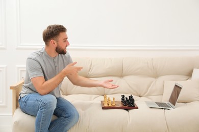 Photo of Young man playing chess with partner through online video chat at home