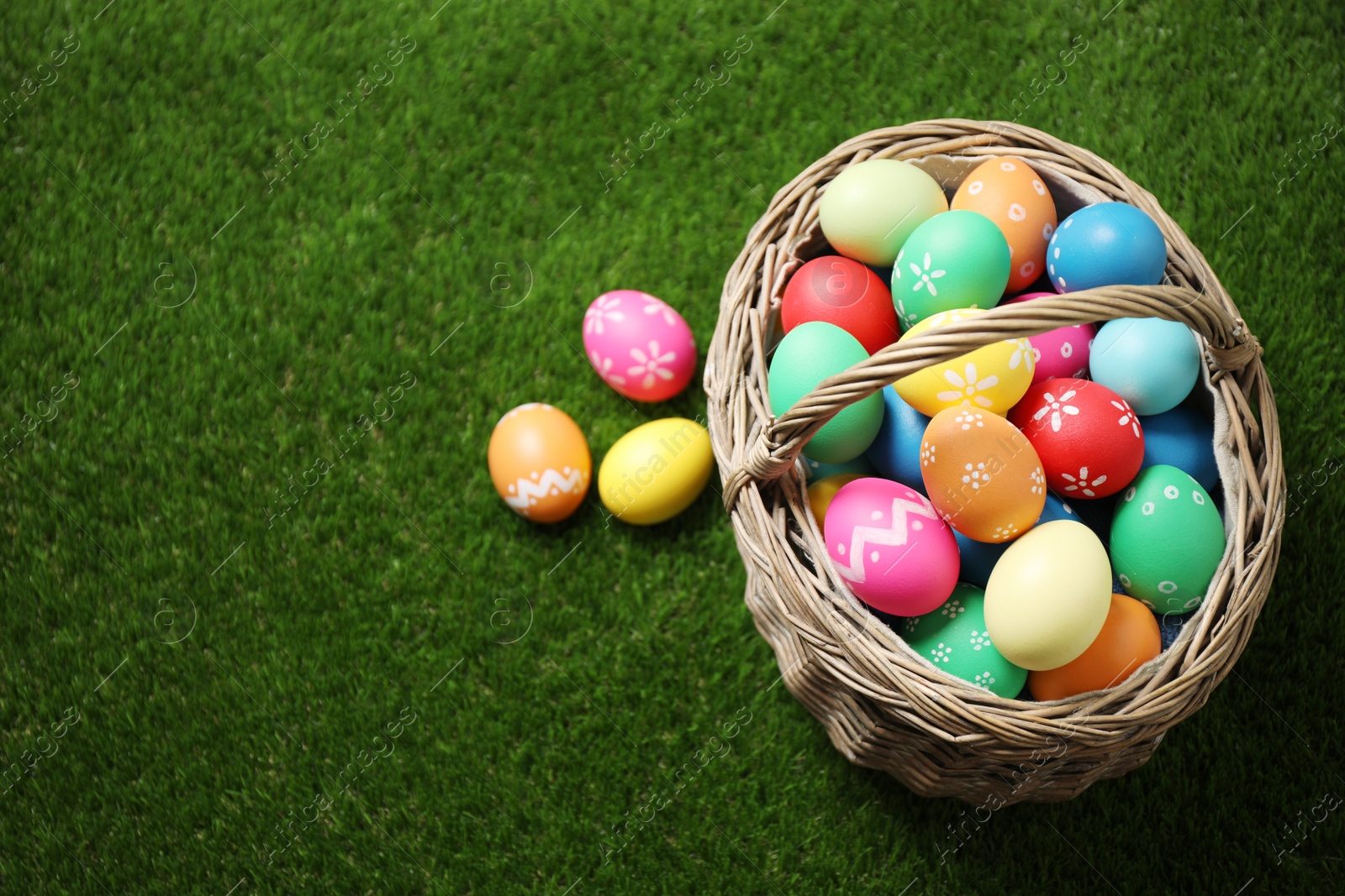 Photo of Colorful Easter eggs in basket on green grass, above view. Space for text