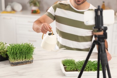 Teacher with microgreens and watering can conducting online course in kitchen, closeup. Time for hobby