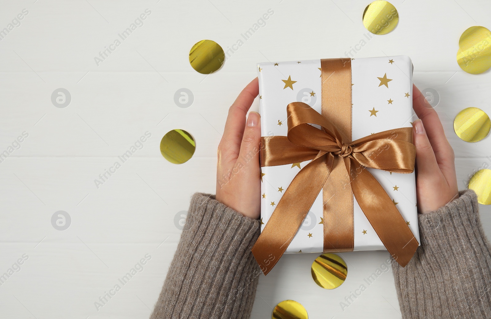 Photo of Woman with Christmas gift and confetti at white wooden table, top view. Space for text