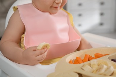 Cute little baby wearing bib while eating at home, closeup