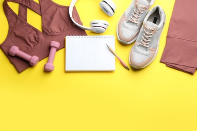 Photo of Flat lay composition with sportswear, notebook and dumbbells on yellow background, space for text. Gym workout plan