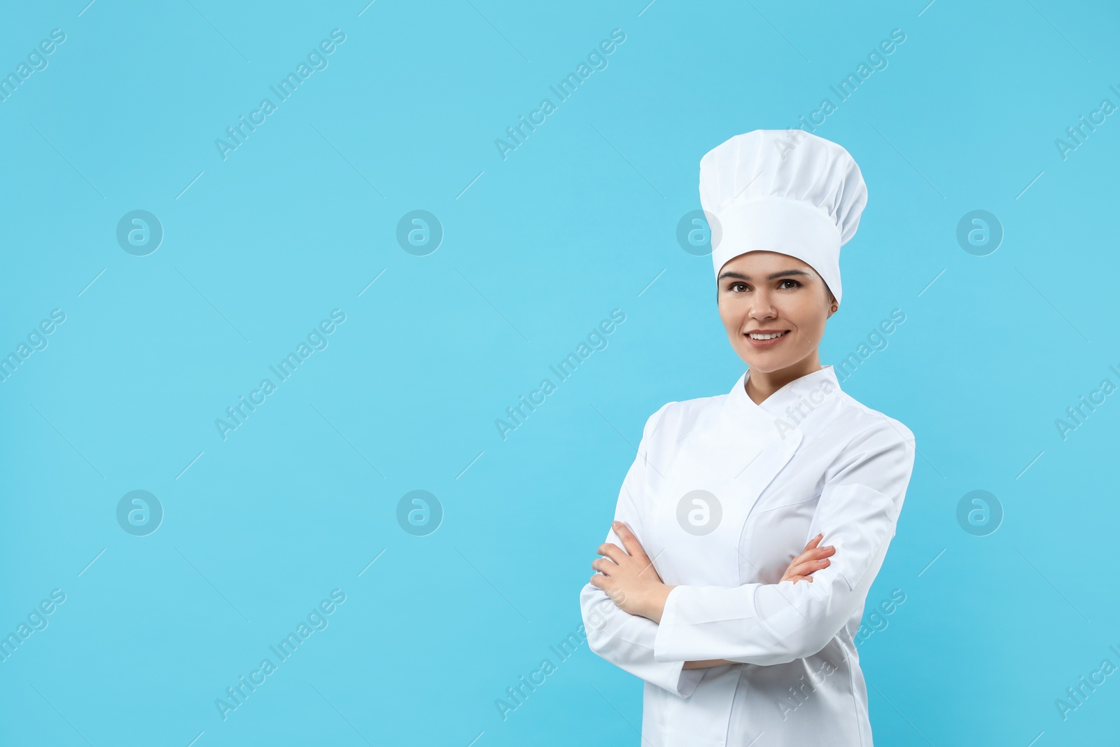 Photo of Happy female chef wearing uniform and cap on light blue background. Space for text