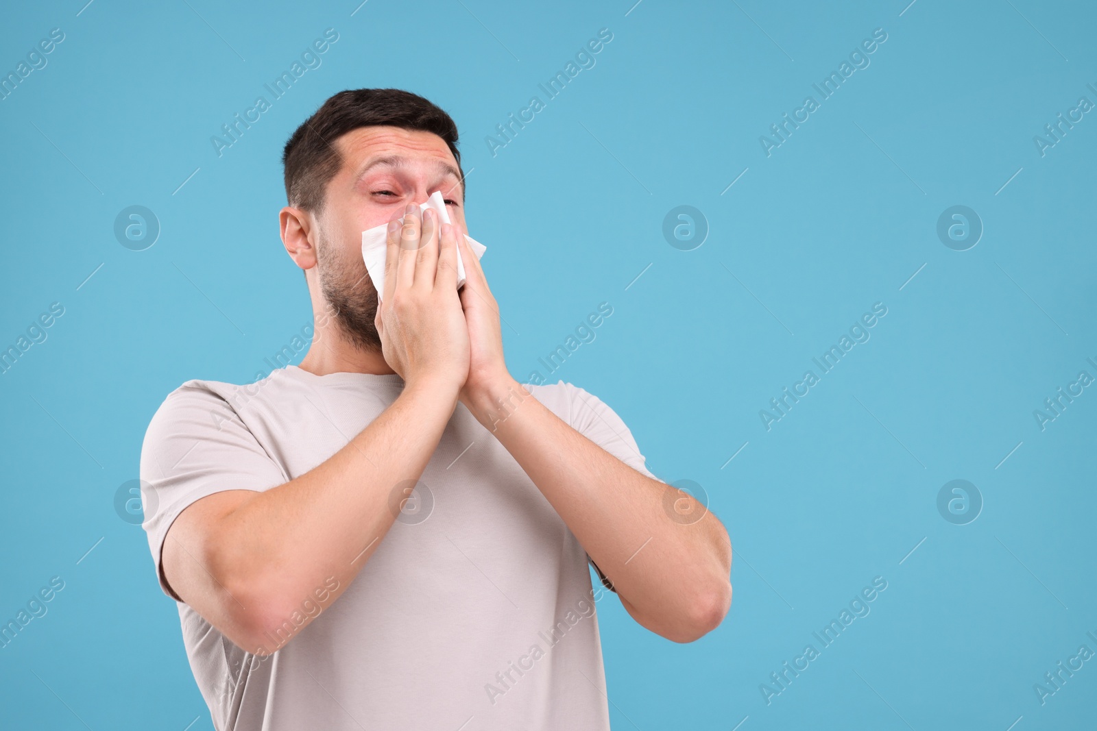 Photo of Allergy symptom. Man sneezing on light blue background. Space for text