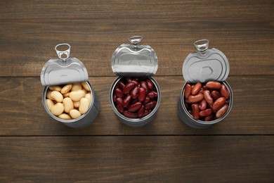 Photo of Tin cans with different canned kidney beans on wooden table, flat lay