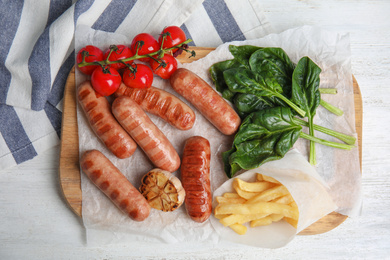 Tasty grilled sausages served on white wooden table, flat lay