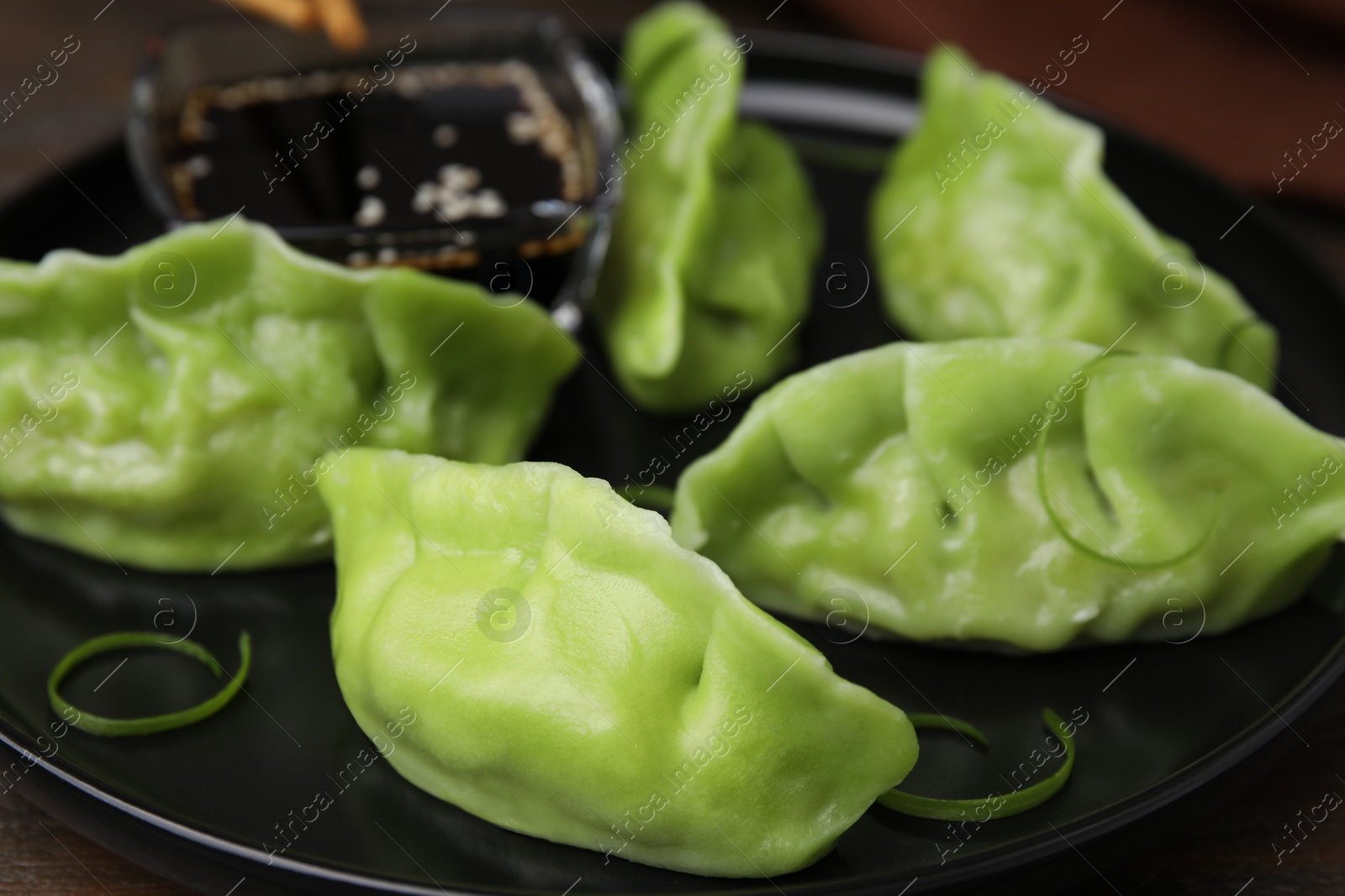 Photo of Delicious green dumplings (gyozas) and soy sauce on plate, closeup