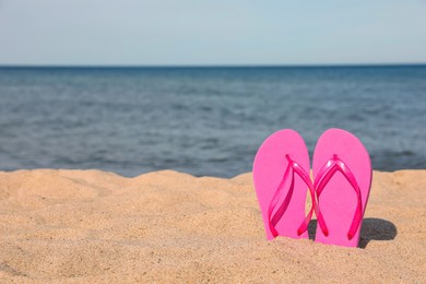 Photo of Stylish pink slippers on sand near sea, space for text. Beach accessory