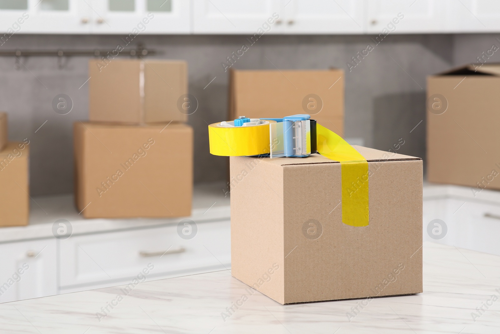 Photo of Box and adhesive tape dispenser in kitchen, space for text