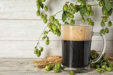 Photo of Composition with tasty beer, wheat spikes and fresh green hops on wooden table. Space for text