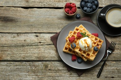 Delicious Belgian waffles with ice cream, berries and caramel sauce served on wooden table, flat lay. Space for text