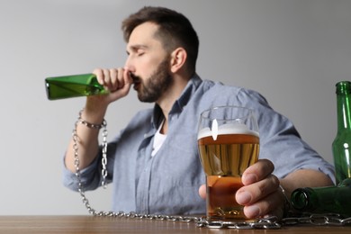 Photo of Addicted man chained to alcoholic drink at wooden table, focus on hand