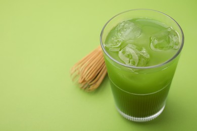 Glass of delicious iced matcha tea and bamboo whisk on green background, closeup. Space for text