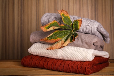 Photo of Stack of folded knitted sweaters and autumn leaf on table against wooden background