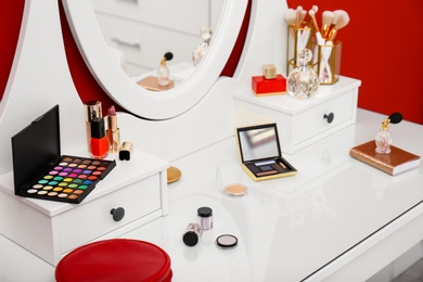 Photo of Different makeup products and bottles of perfumes on white dressing table