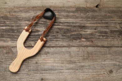 Photo of Slingshot with pebble on wooden background, top view. Space for text