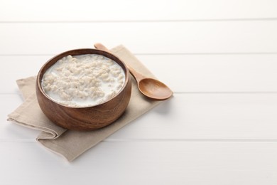 Photo of Tasty boiled oatmeal in bowl and spoon on white wooden table, space for text