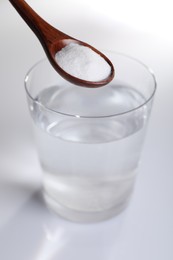 Photo of Spoon with baking soda over glass of water on white background, closeup