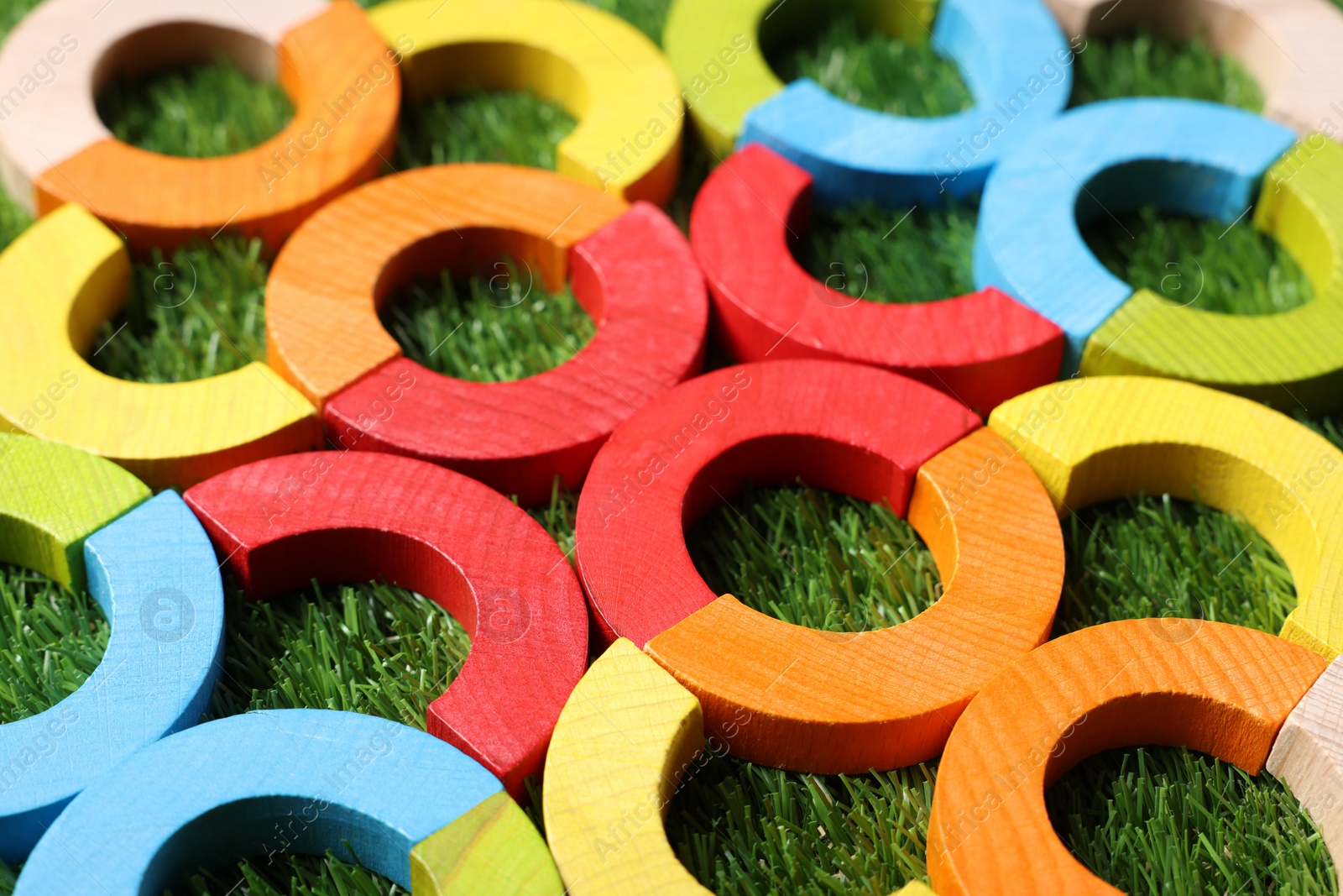 Photo of Colorful wooden pieces of play set on green grass, closeup. Educational toy for motor skills development