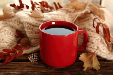 Photo of Cup of hot drink, knitted scarf and autumn leaves on wooden table. Cozy atmosphere