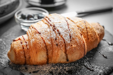 Photo of Tasty croissant with sauce and sugar powder on slate plate, closeup