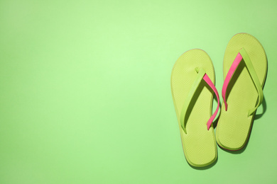 Pair of stylish flip flops on green background, top view with space for text. Beach objects