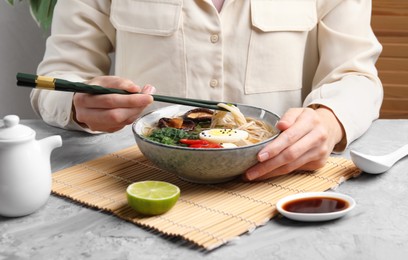Photo of Woman eating delicious ramen with chopsticks at grey table, closeup. Noodle soup